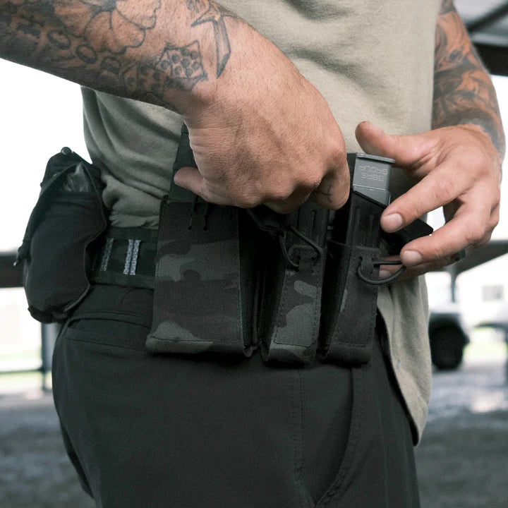 Tattooed man drawing a pistol magazine from a multicam black MOLLE double mag pouch worn on a belt.