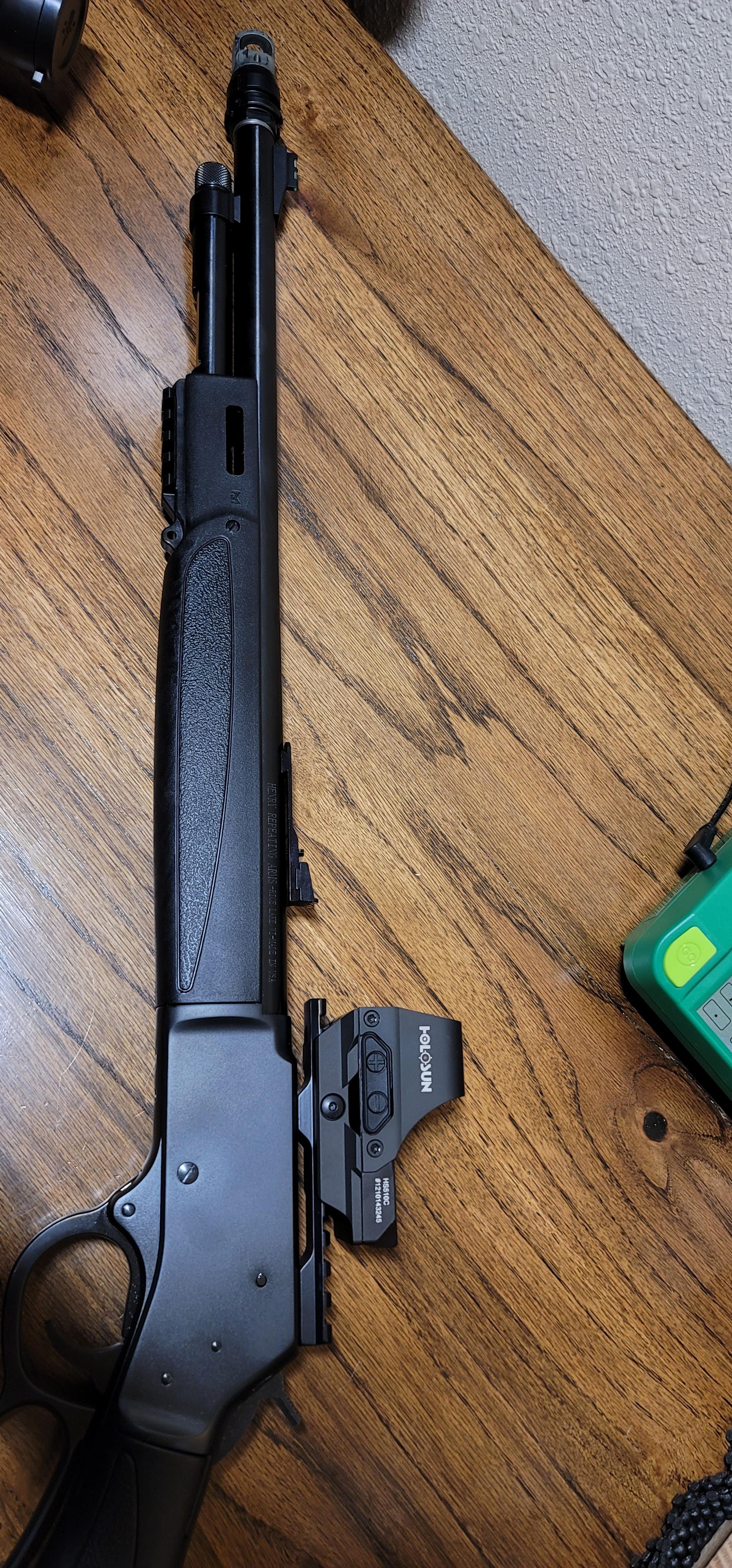 Henry lever-action carbine lying on a wooden surface with a Holosun red dot sight mounted low on the receiver, shown next to its mount.