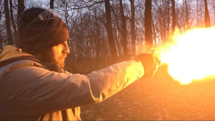 Person firing a handgun outdoors at dusk with a large muzzle flash visible at the barrel