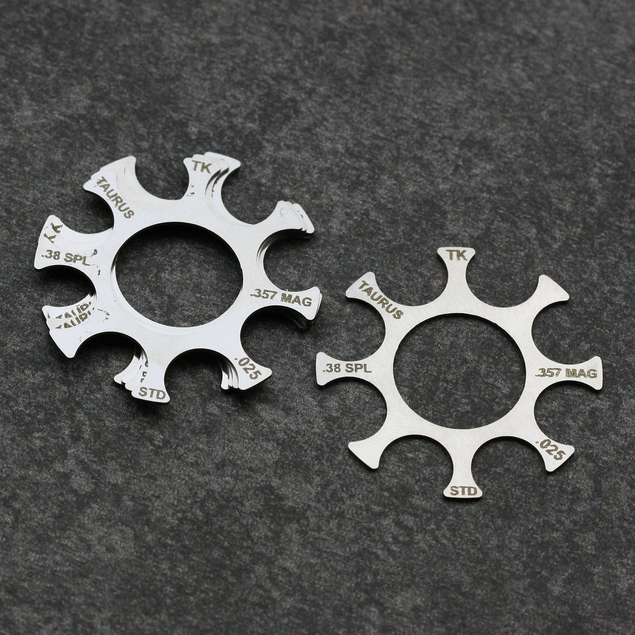 Two stainless steel Taurus moon clips for .38 Special and .357 Magnum revolvers on a gray surface