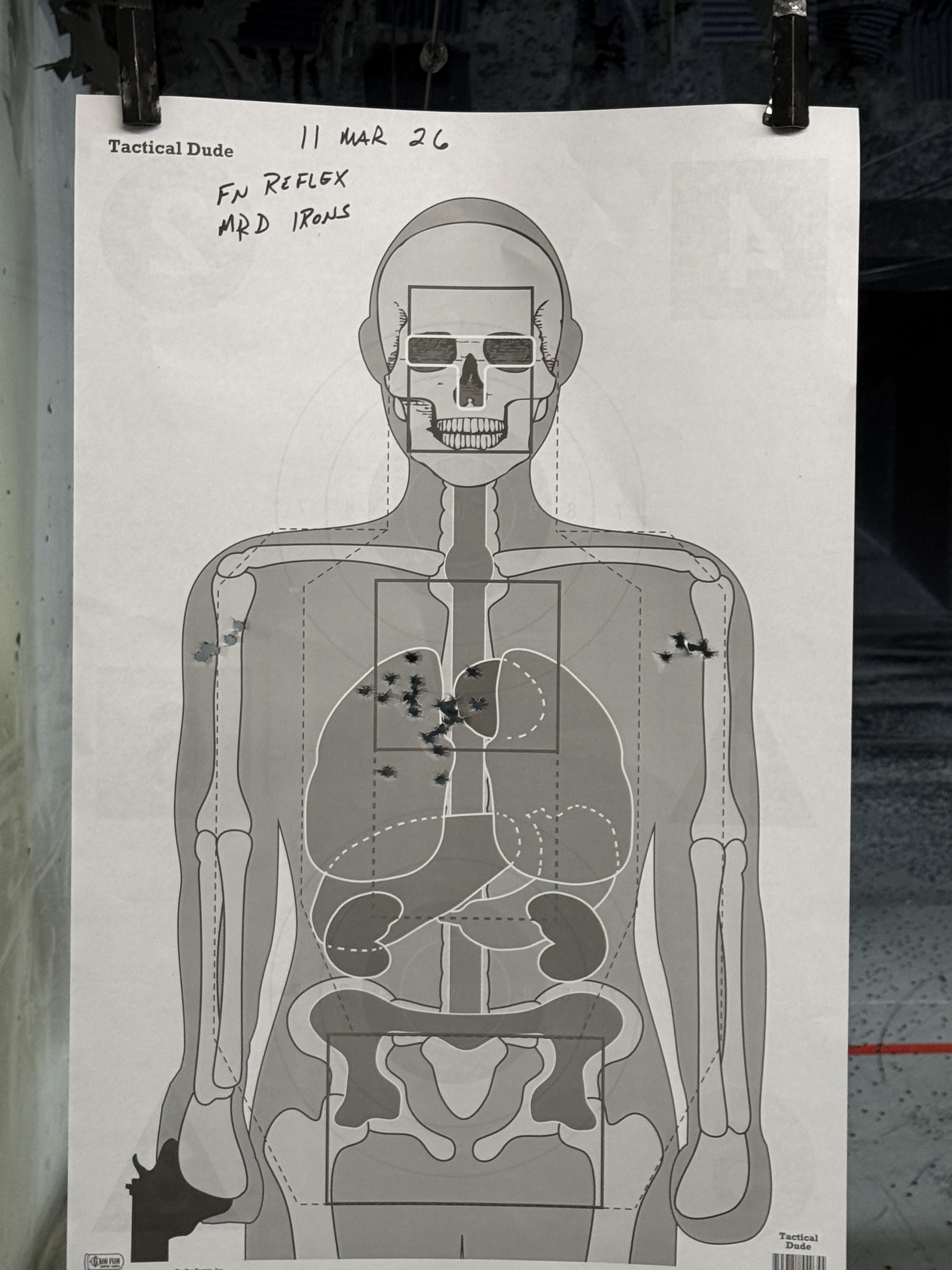 Anatomical silhouette target with bullet holes clustered in the chest cavity, handwritten notes reading FN Reflex MRD Irons dated 11 Mar 26.
