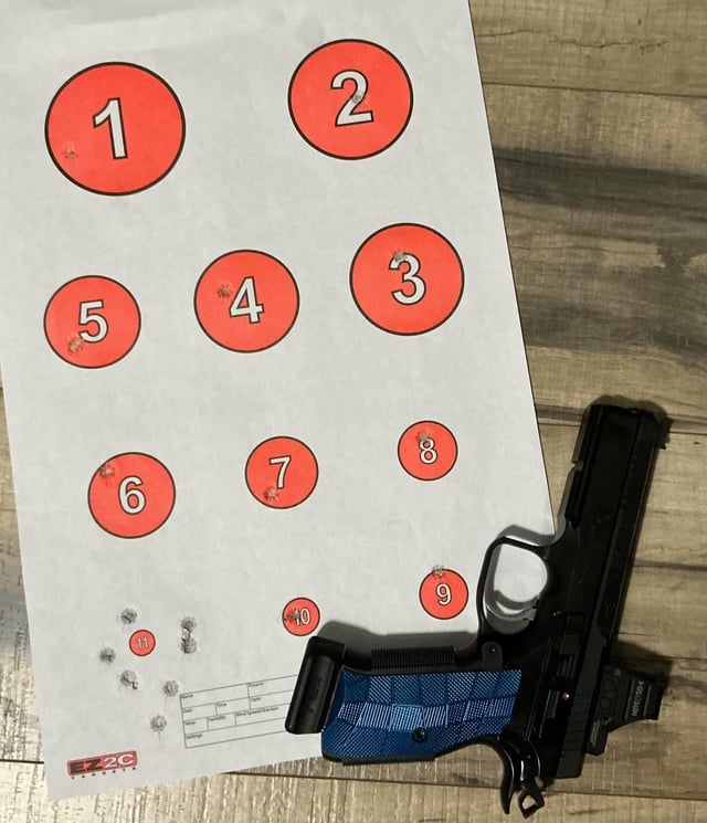 A numbered red circle shooting target with bullet holes laid on a wooden surface next to a CZ semi-automatic pistol with a blue grip.