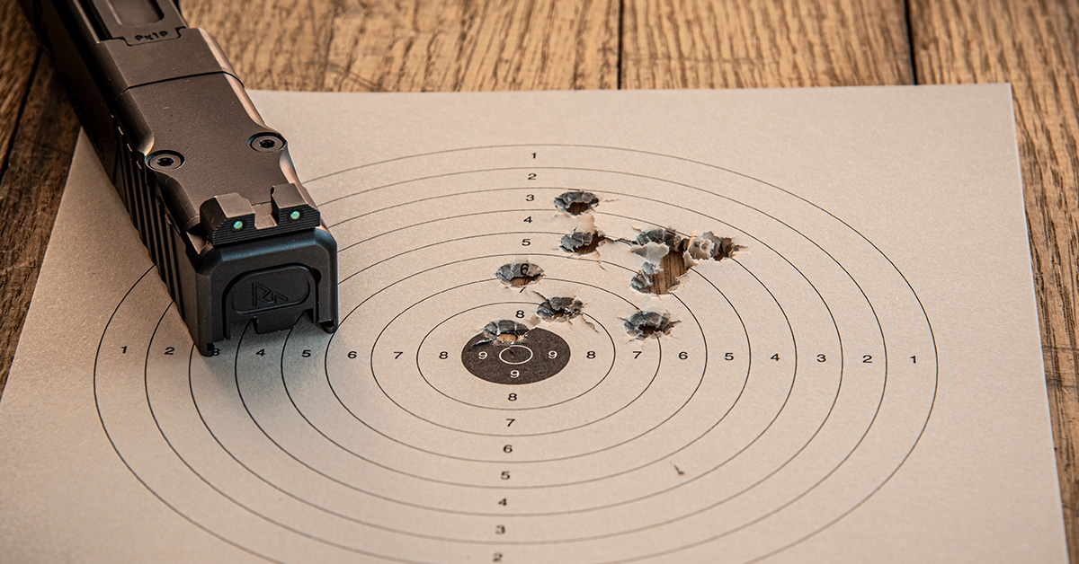 Springfield XD-series pistol slide with fiber optic sights resting on a paper bullseye target with multiple bullet holes clustered in the 6-9 ring area.
