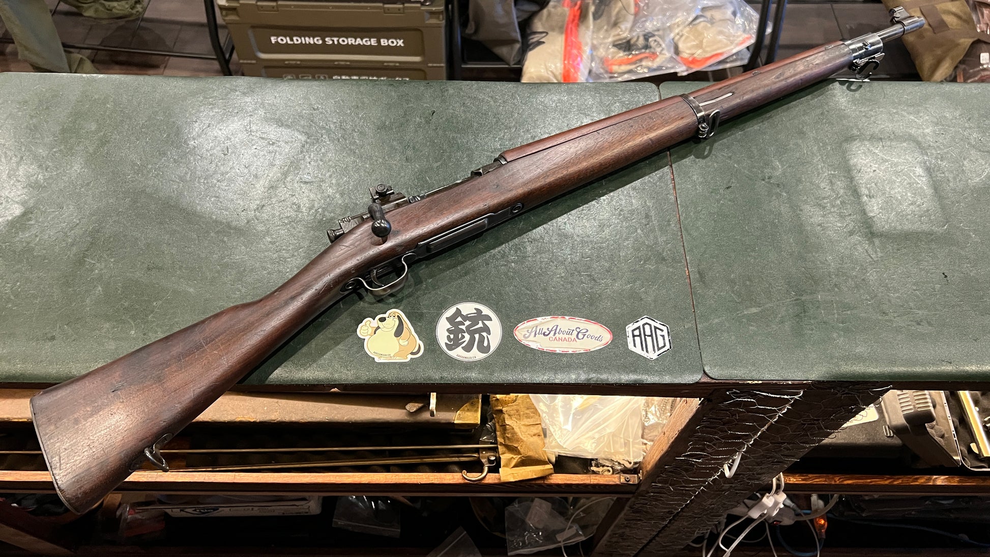 M1 Garand rifle with worn walnut stock laid flat on a green surface, showing overall use wear consistent with a surplus shooter-grade example.