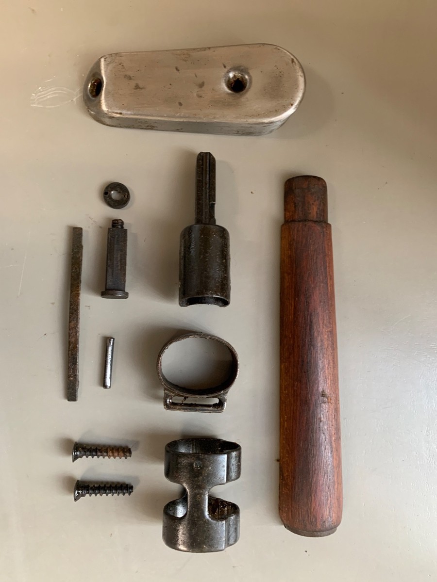 Disassembled milsurp rifle parts laid out on a flat surface, including two barrel bands, a wooden forestock handguard, a buttplate, pins, screws, and a cleaning rod or similar rod component.