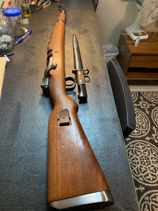 Yugoslav M48 Mauser bolt-action rifle with bayonet resting on a workbench, showing walnut stock and receiver.