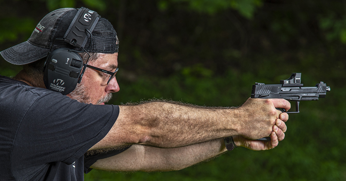Shooter in isosceles stance firing a Taurus TX22 pistol equipped with a red dot optic at an outdoor range.
