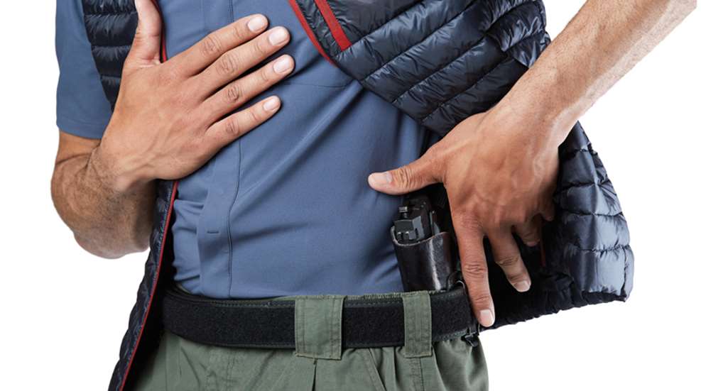 Man lifting a puffer vest to draw a pistol from an IWB holster on his right hip