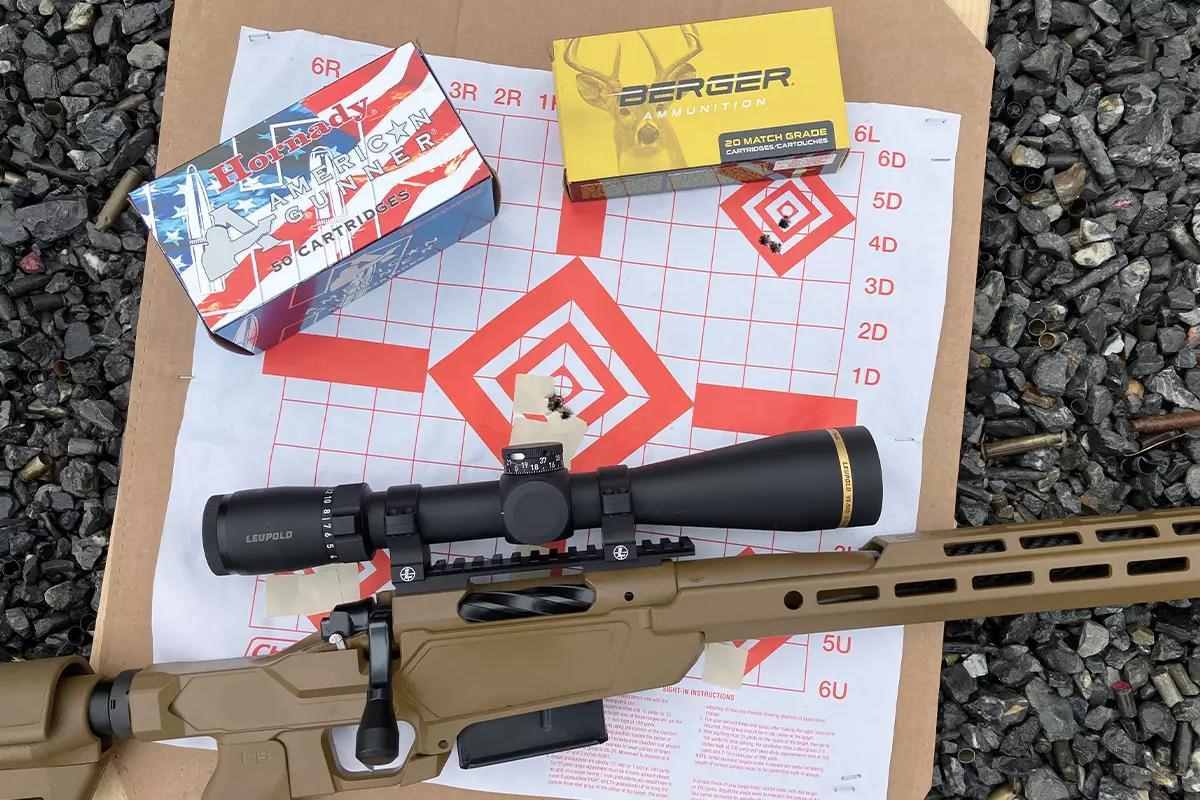Tan chassis bolt-action rifle with Leupold scope on a shooting target, with boxes of Hornady American Gunner and Berger Match Grade ammunition nearby.
