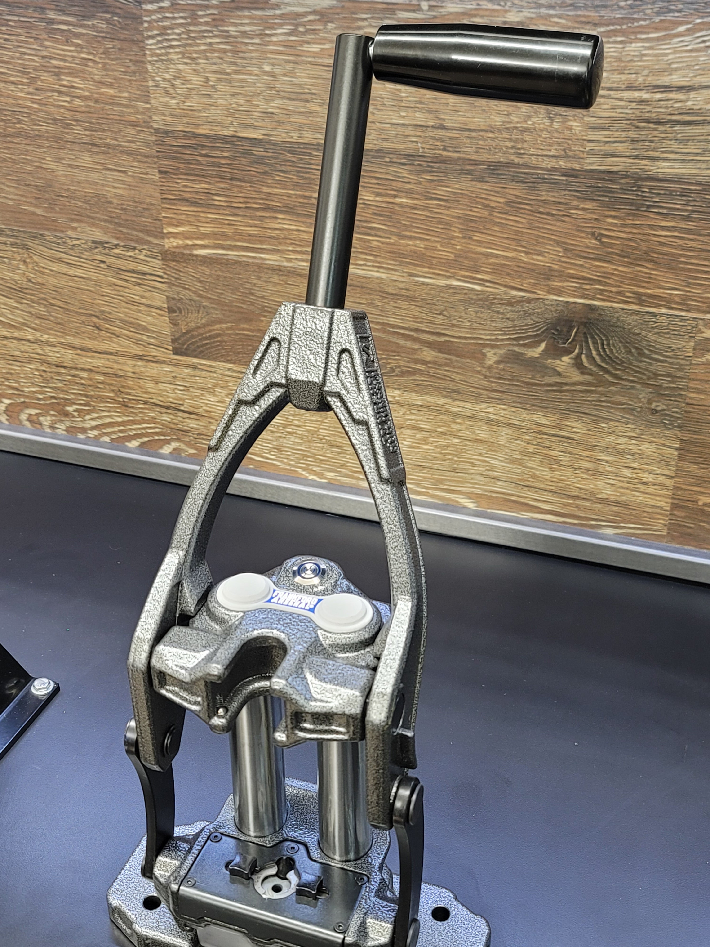 Frankford Arsenal M-Press single stage reloading press with dual guide rods and crank handle, mounted on a base plate on a dark surface.