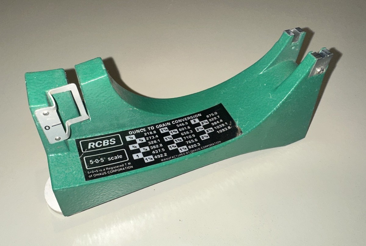 Green cast metal base of an RCBS 5-0-5 beam scale with a black ounce-to-grain conversion label and two metal beam adjustment brackets.