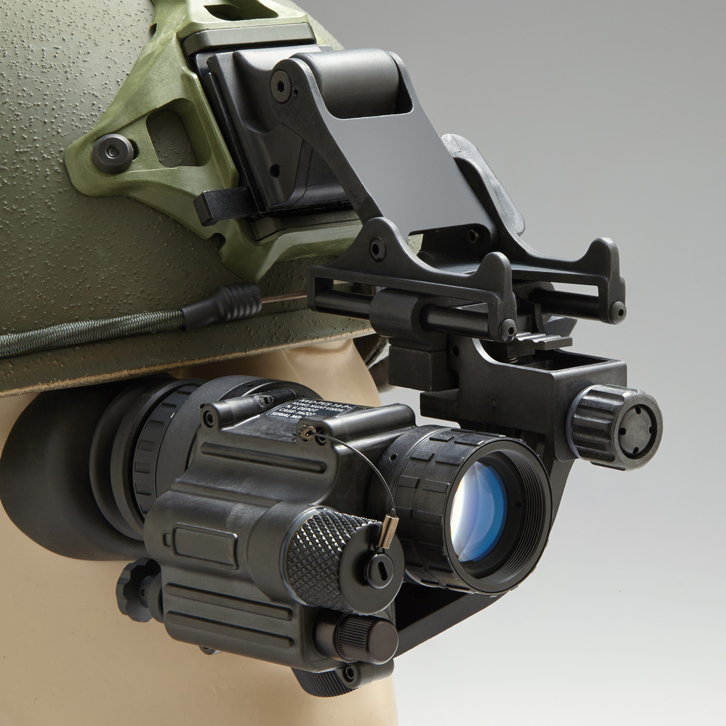 AN/PVS-14 night vision monocular attached to a green military helmet via a J-arm rhino mount, shown in the deployed position in front of the helmet.