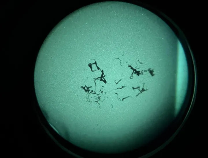 Close-up view through a circular optic lens showing dark scratches and debris on the lens surface against a green-tinted background.