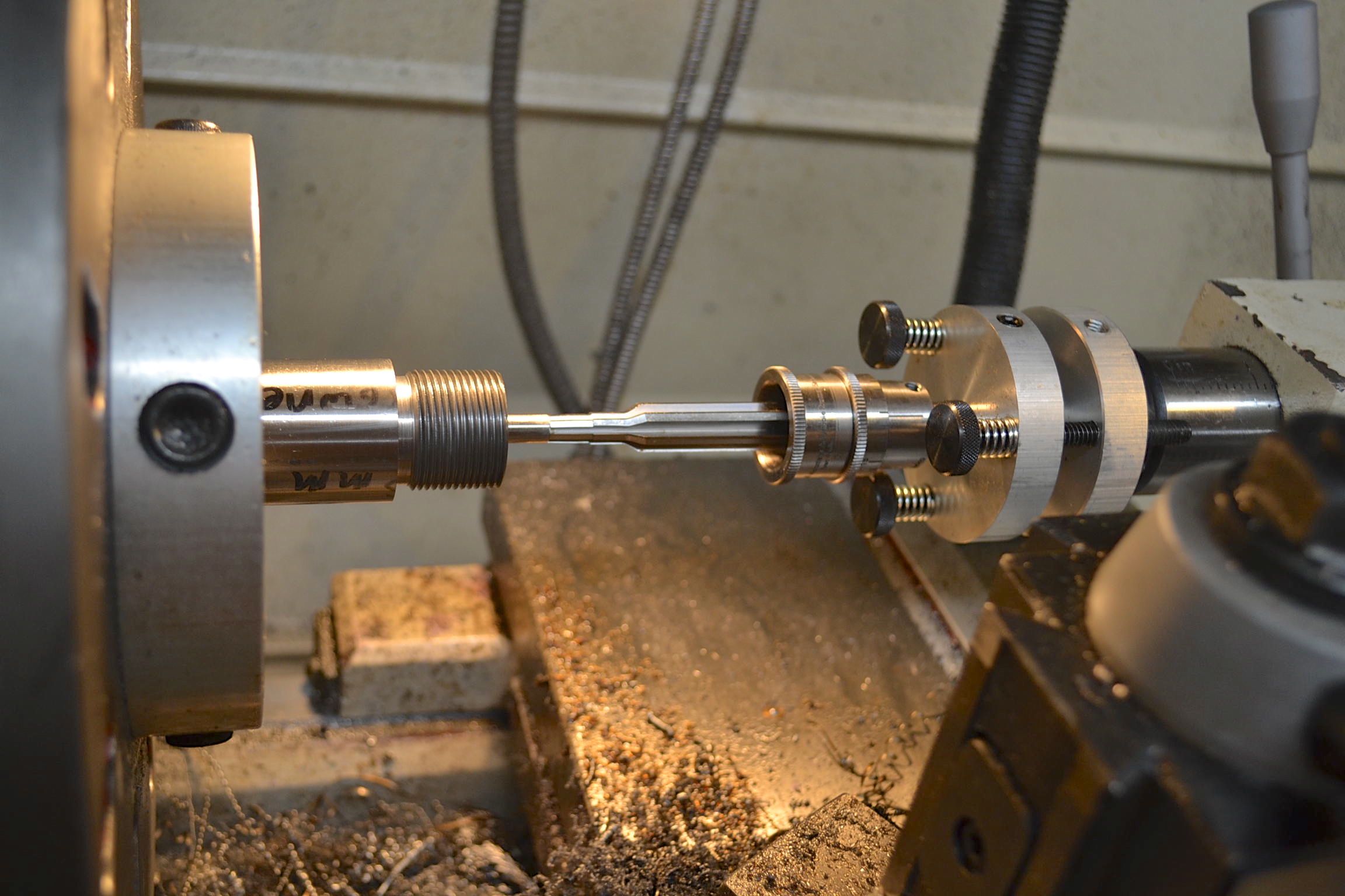 Chamber reamer held in a metal lathe between a faceplate and steady rest, with metal shavings on the lathe bed below.