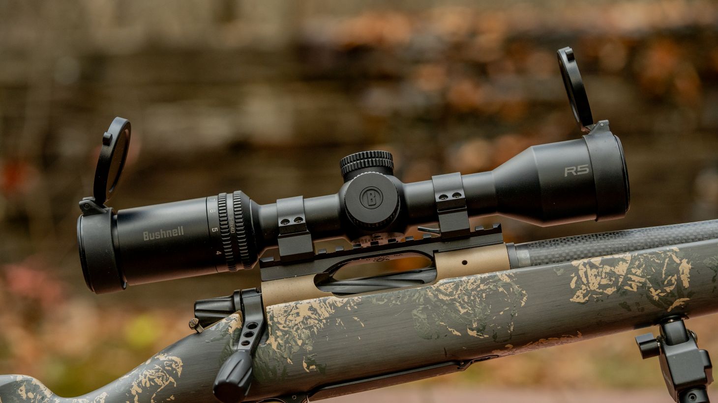 Bushnell R5 riflescope mounted on a bolt-action rifle with a camouflage carbon fiber stock and bipod, photographed outdoors.