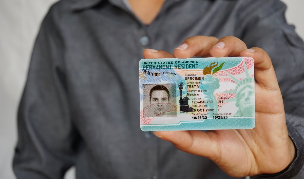 Person holding a U.S. Permanent Resident specimen card facing the camera.