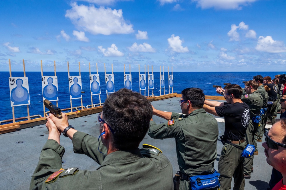 Navy personnel shooting pistols at numbered silhouette targets on a ship deck during a qualification exercise.