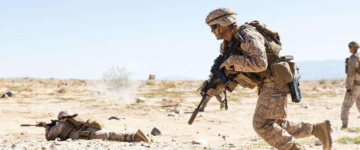 U.S. Marines in desert camouflage conduct live-fire movement drills in an arid training environment.