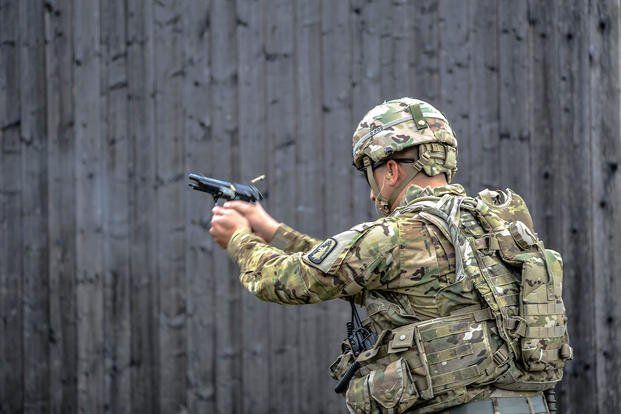 Soldier in OCP uniform and helmet fires a pistol at a range during military marksmanship training.