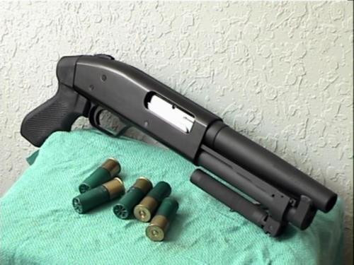 Serbu Super Shorty pump-action AOW shotgun with pistol grip displayed on a green cloth surface next to five 12-gauge shotgun shells.