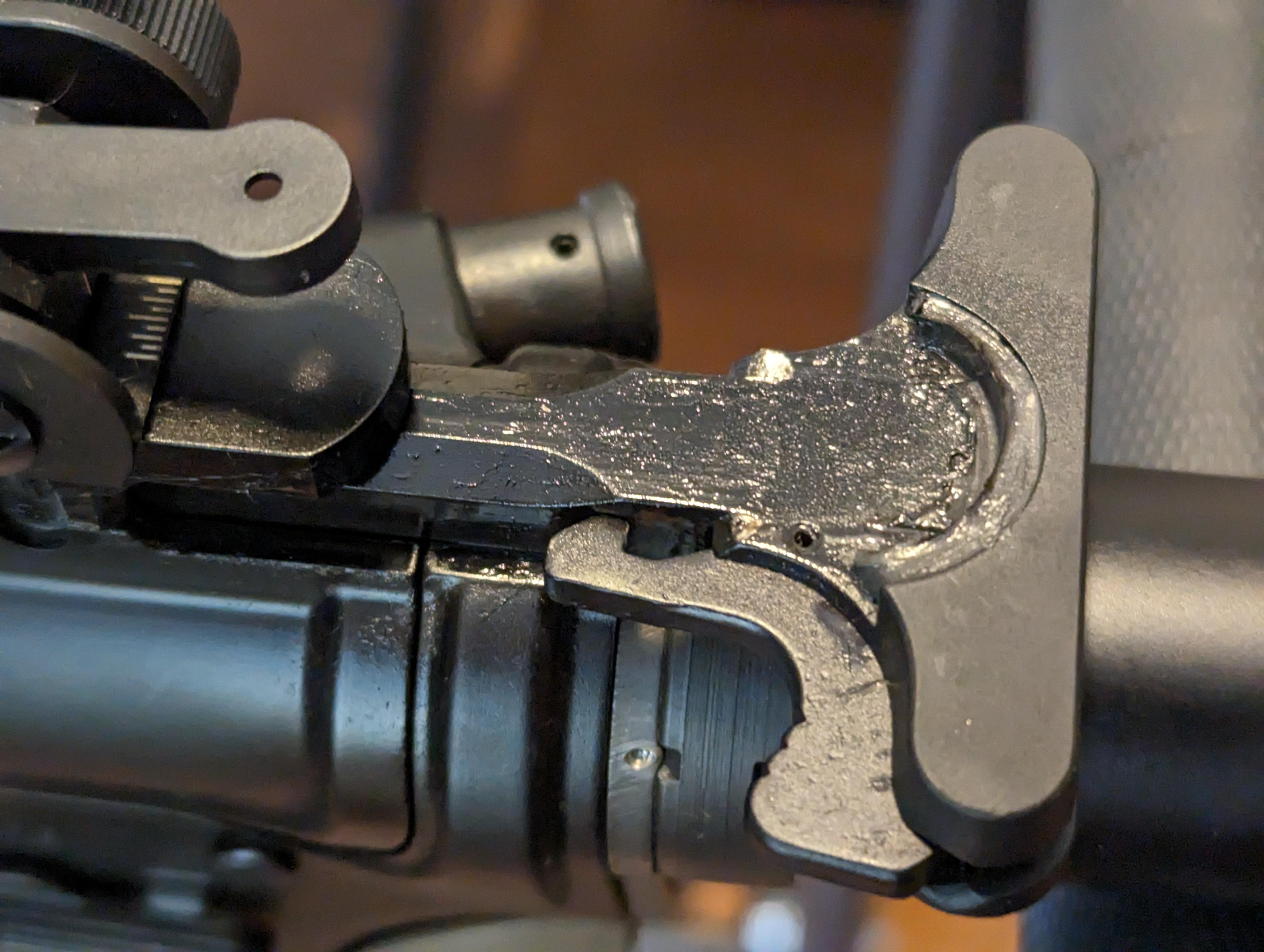 Close-up of a damaged AR-15 charging handle with visible cracking and gas fouling at the latch area, mounted on an upper receiver.