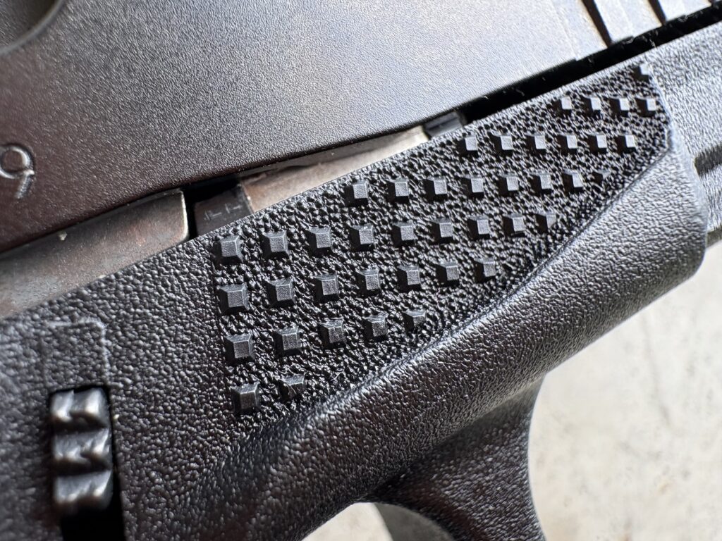 Close-up of raised square checkering pattern machined into the aluminum grip frame of a Beretta B22 Jaguar pistol.