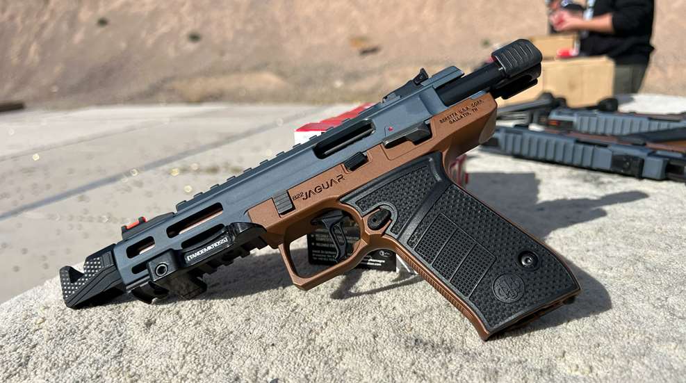 Beretta B22 Jaguar rimfire pistol in gray and flat dark earth finish resting on a concrete surface at an outdoor range, showing TandemKross rail mount and fiber optic front sight.