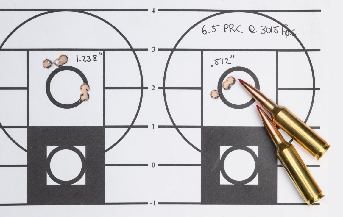 Shooting target showing two groups side by side, labeled 1.238 inches and 0.512 inches, with two 6.5 PRC cartridges resting on the target near the tighter group.