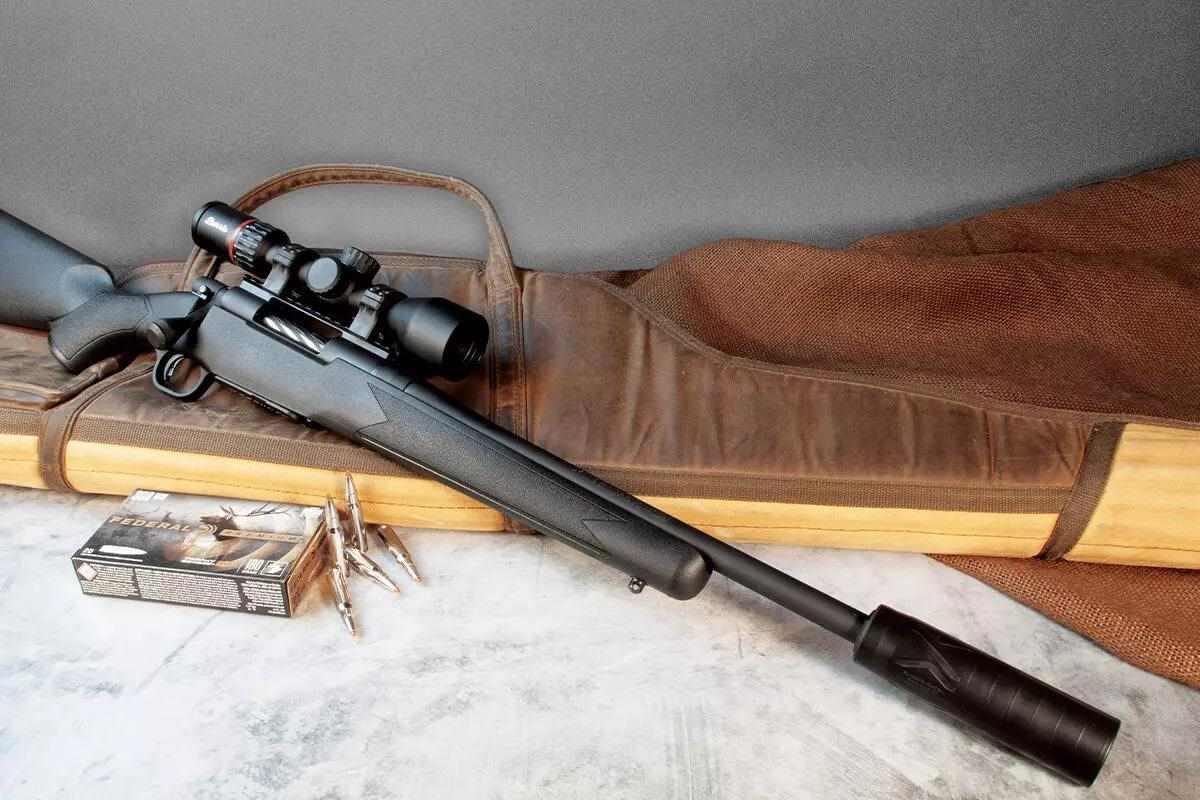 Suppressed bolt-action hunting rifle with scope, Federal ammo box, and loose cartridges on a rifle case