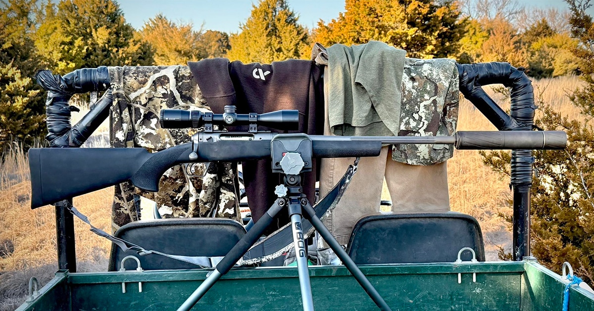 Bolt-action rifle on a BOG tripod shooting rest mounted on a hunting vehicle in a field setting.