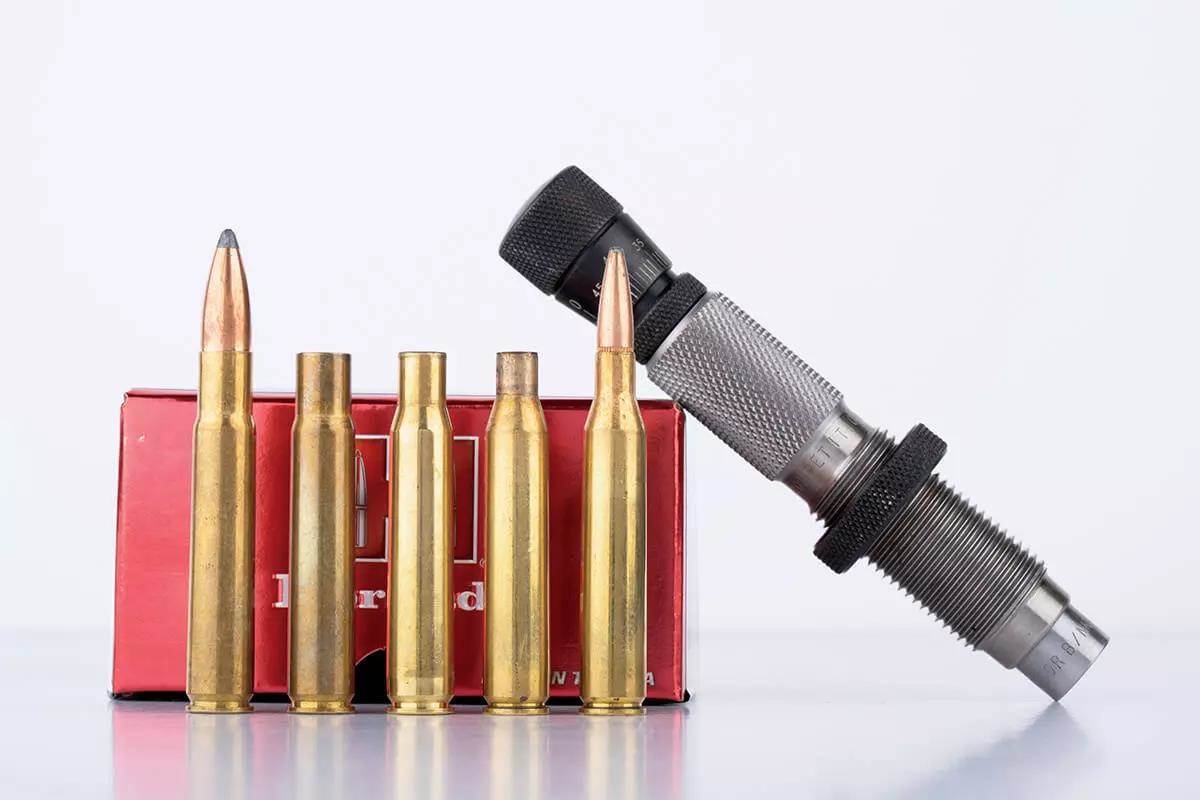 Four .260 Remington cartridges and brass cases leaning against a red Hornady box, with a reloading seating die propped beside them on a white surface.