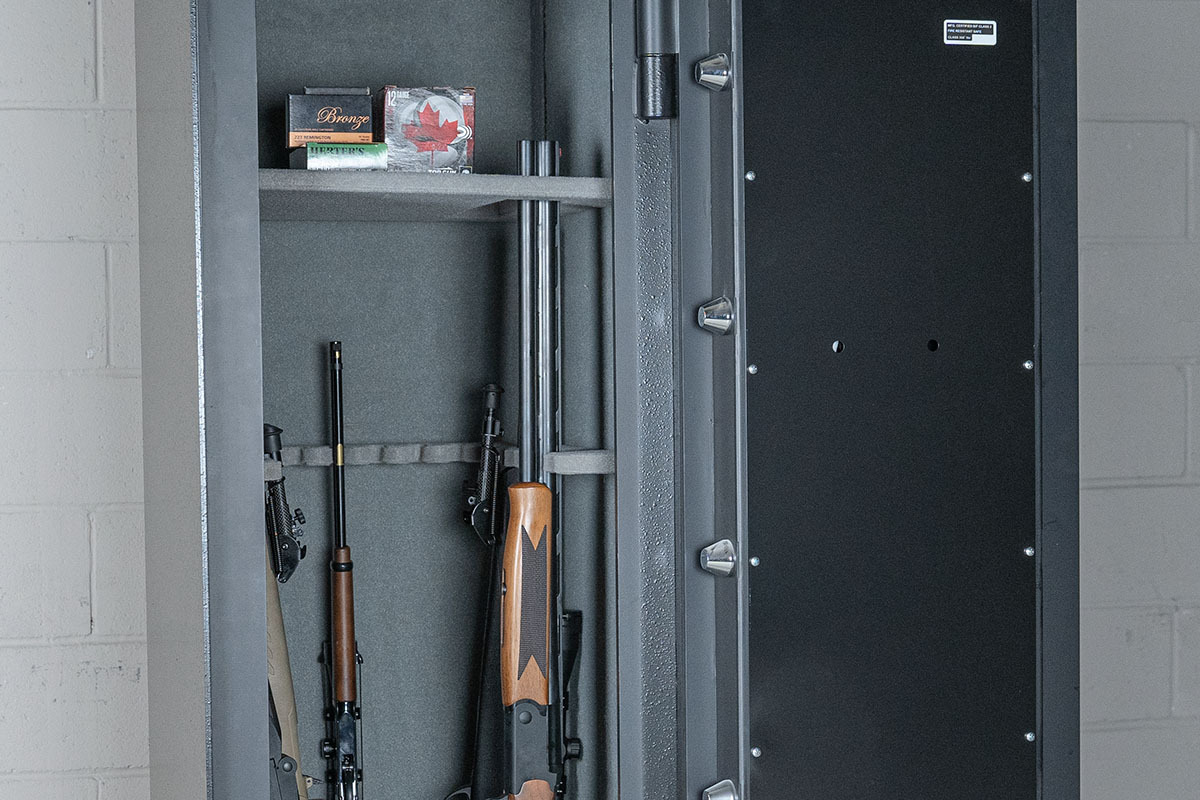 Open gun safe containing multiple rifles and boxes of .223 Remington ammunition on upper shelf