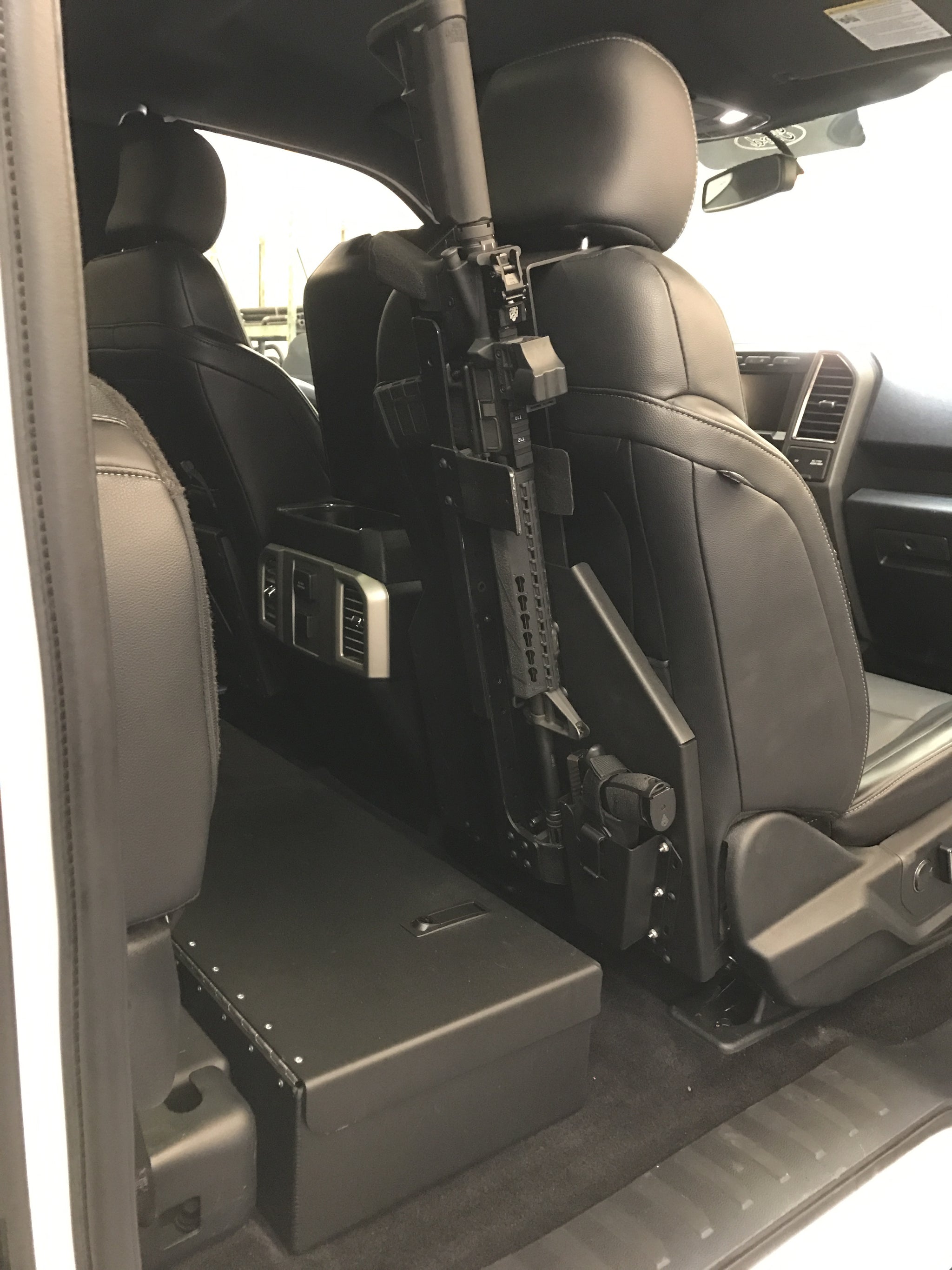 AR-style rifle mounted on a vertical between-seat rack inside a truck cab