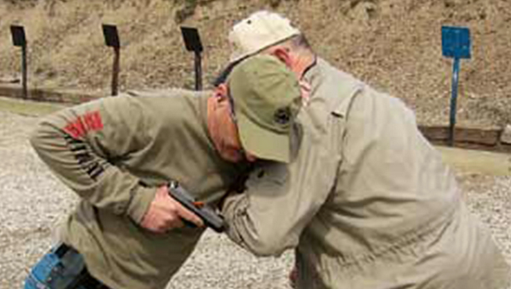 German soldier in flecktarn camo aims a belt-fed machine gun from behind cover with NV helmet and red ballistic glasses.