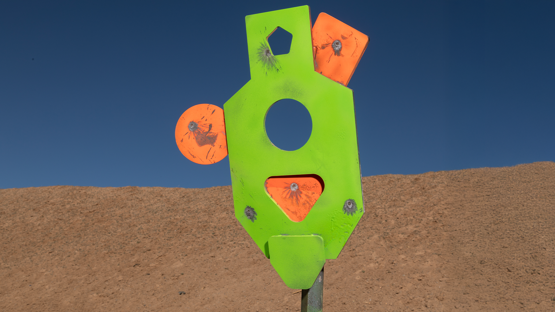 Green steel shooting target with orange geometric zones showing bullet impacts, used for armor-gap training drills