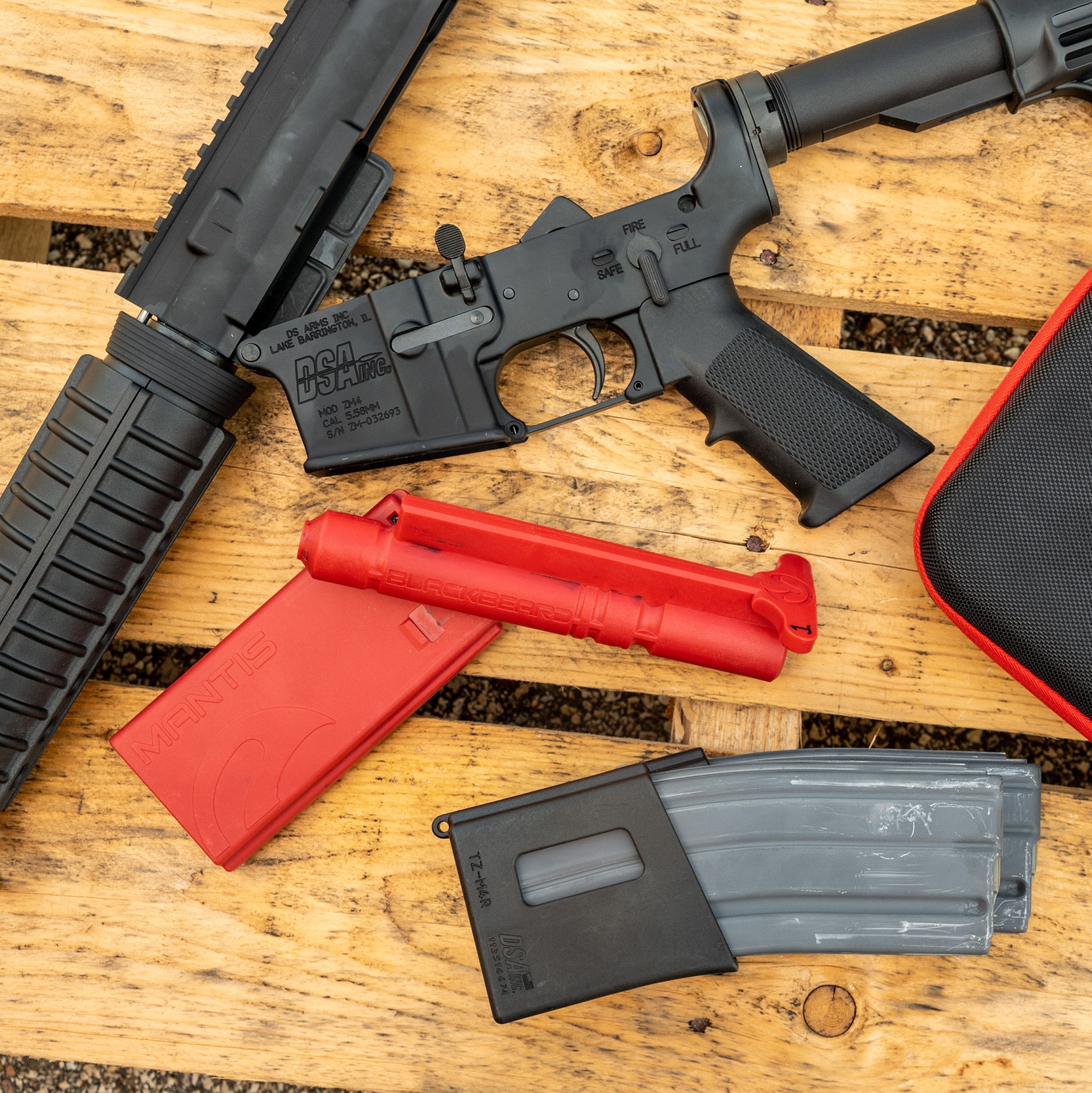 DSA ZM4 AR-15 lower receiver on a wooden pallet surrounded by a red Mantis training magazine, a red Blackbeard trigger system, and gray 30-round AR magazines.