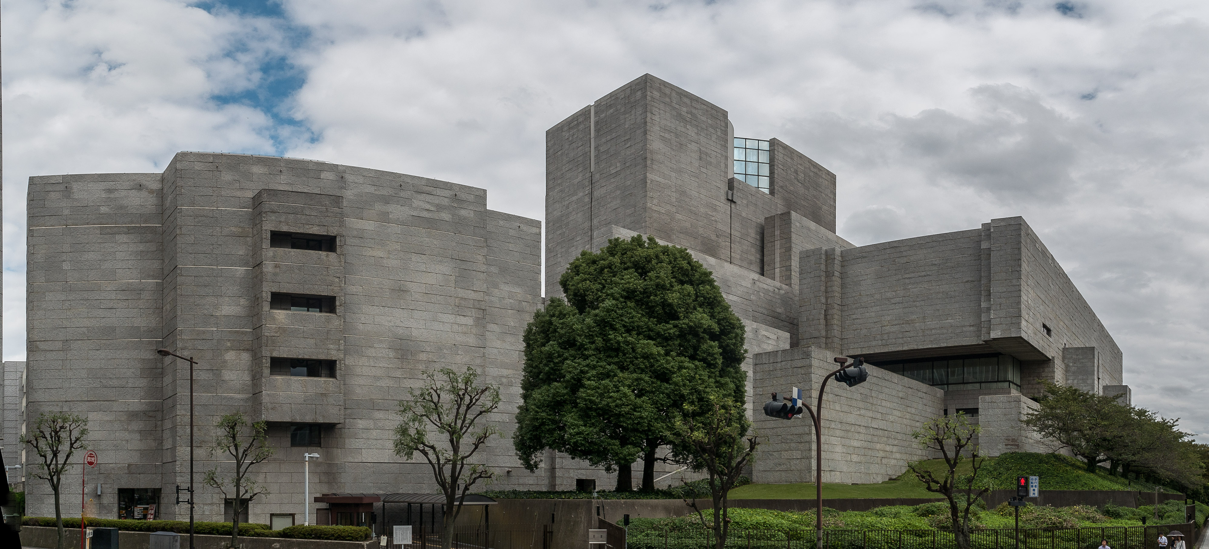 Exterior of a large brutalist concrete government building in Japan, surrounded by trees and landscaping.
