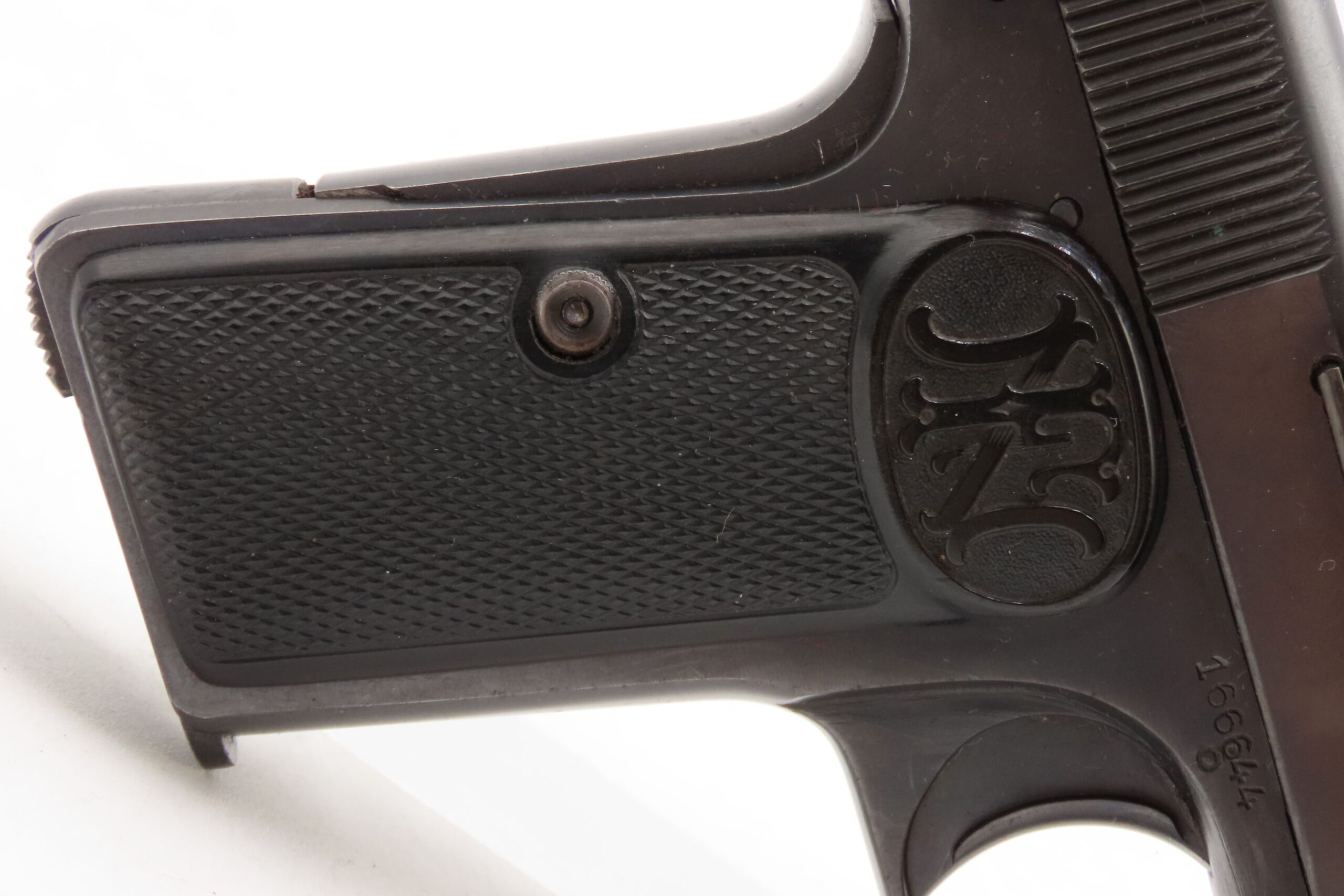 Close-up of the grip panel and frame of an FN Browning Model 1910 pistol, showing checkered black grips with an FN logo medallion and a serial number stamped on the frame.