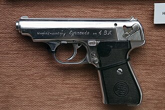Nickel-finished Sauer 38H semi-automatic pocket pistol with black grips, shown in right profile against a museum display background.