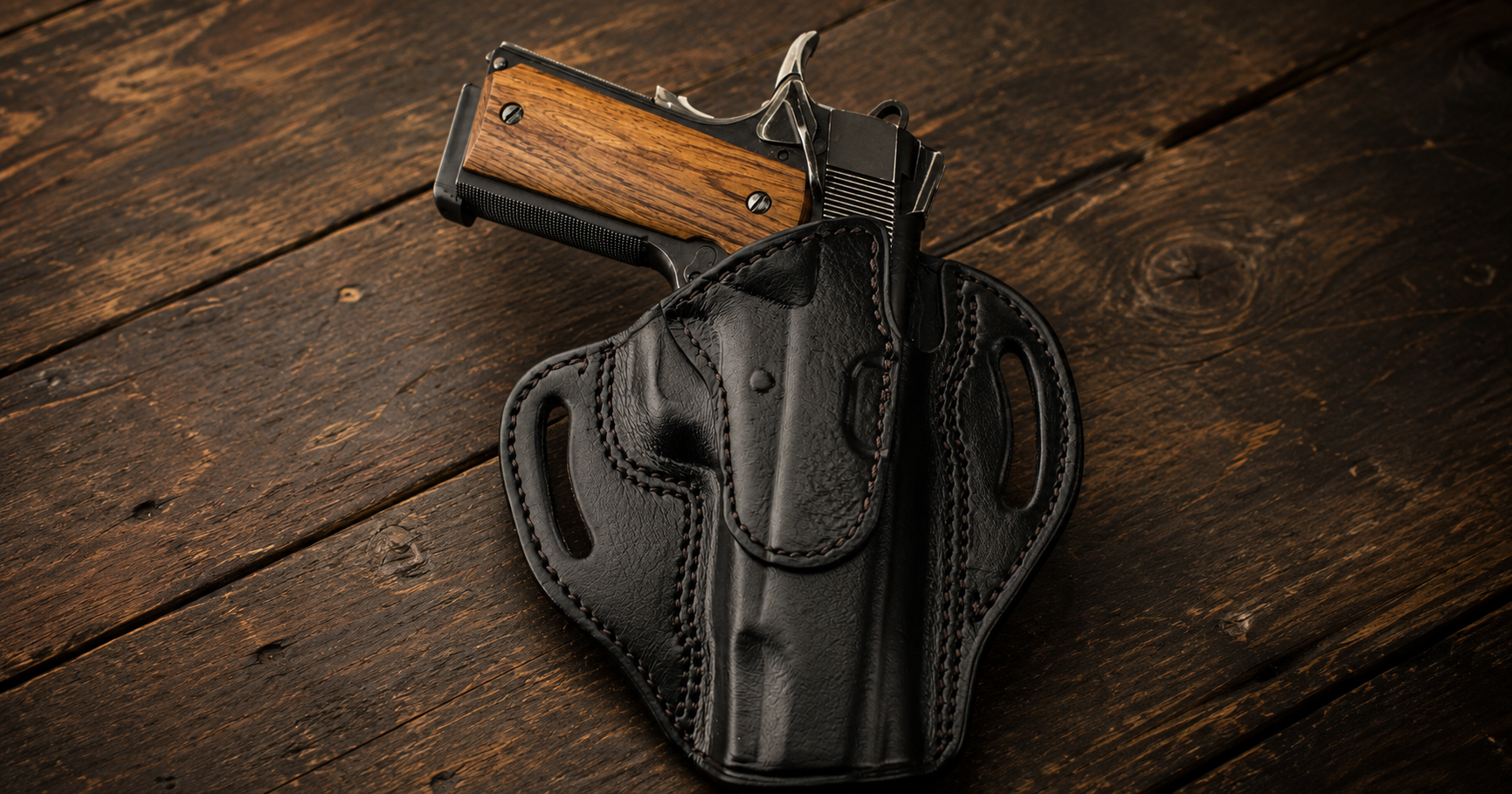 A 1911 pistol with wood grips partially drawn from a black leather OWB holster, laid on a wooden surface.