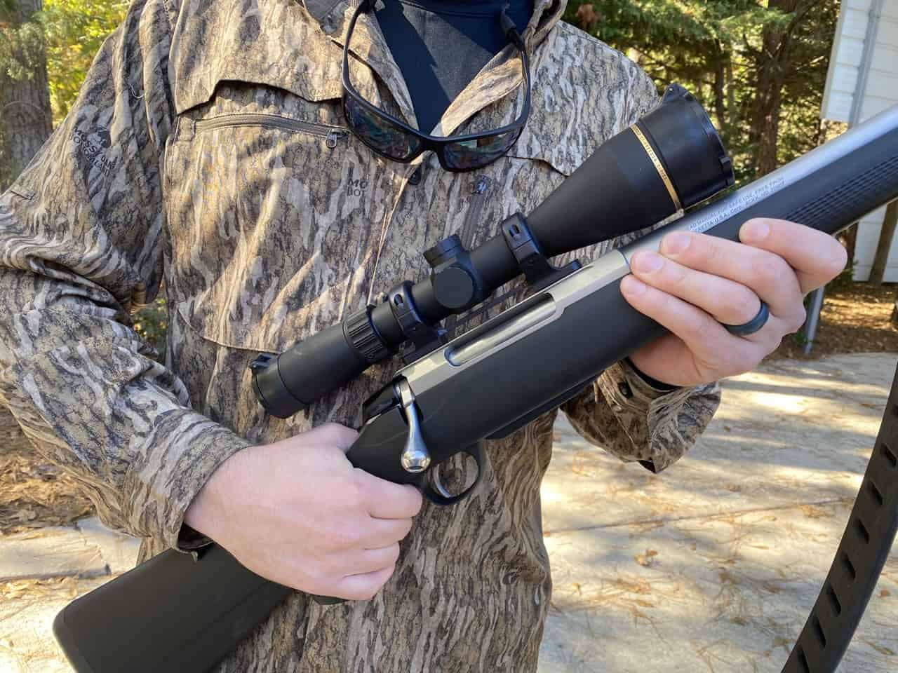 Hunter in camouflage holding a bolt-action rifle with a Leupold riflescope mounted on top.