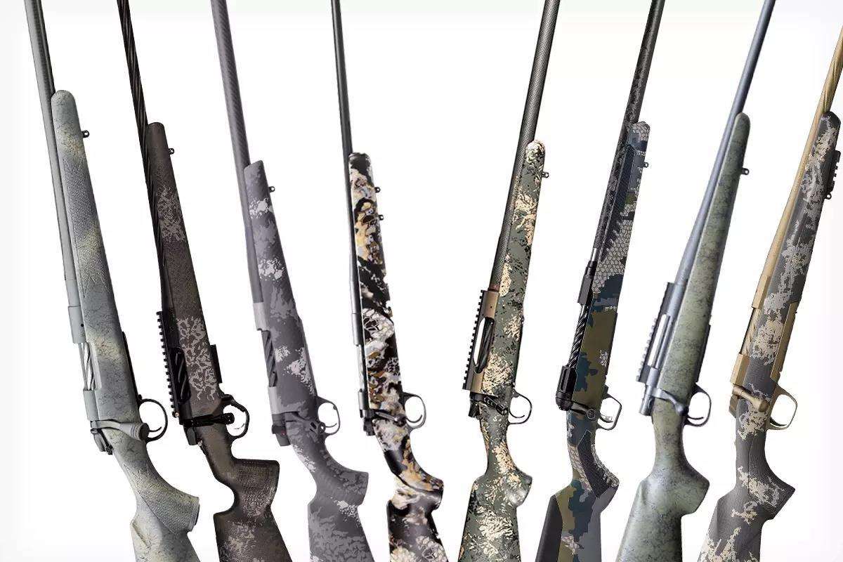 Seven bolt-action hunting rifles displayed side by side in various camouflage and synthetic stock patterns including Sitka, Kuiu, and grey speckle finishes.