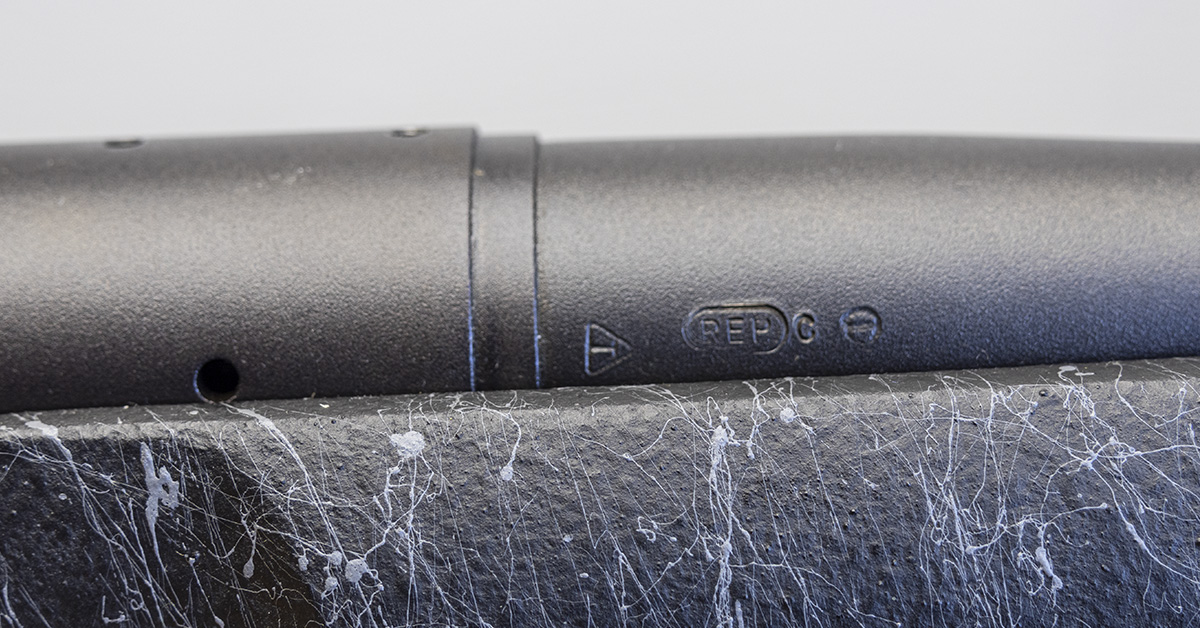 Close-up of stamped markings on a rifle barrel resting on a concrete surface, showing proof marks and manufacturer stamps.