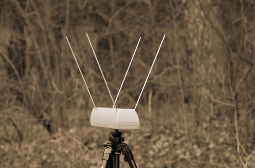 Optical chronograph with three skyscreen rods on a tripod, set outdoors in front of bare winter trees.