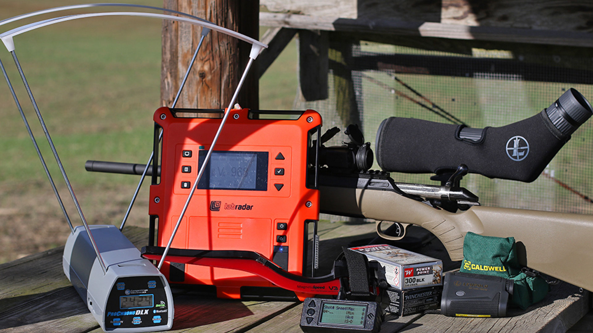 LabRadar, MagnetoSpeed V3, and ProChrono DLX chronographs on a shooting bench with a bolt-action rifle and accessories