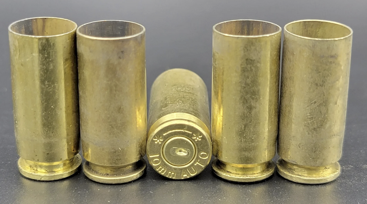 Seven upright spent brass pistol casings on a reflective surface, showing extractor grooves and case heads