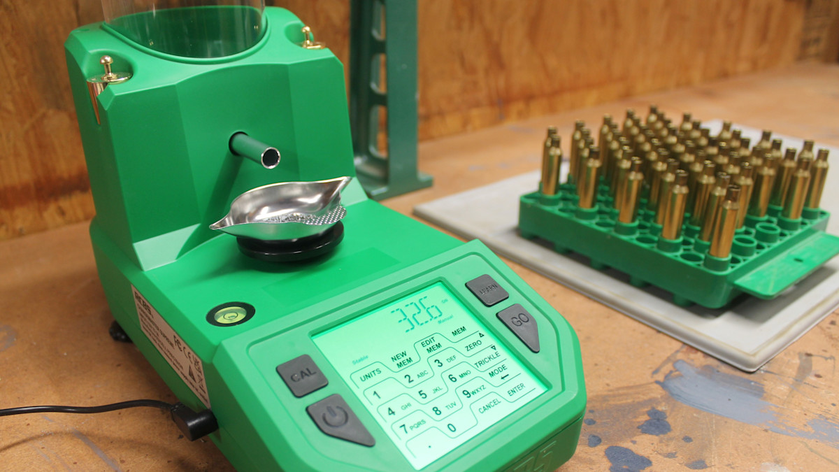RCBS ChargeMaster powder dispenser with LCD readout next to a tray of brass cartridge cases on a reloading bench