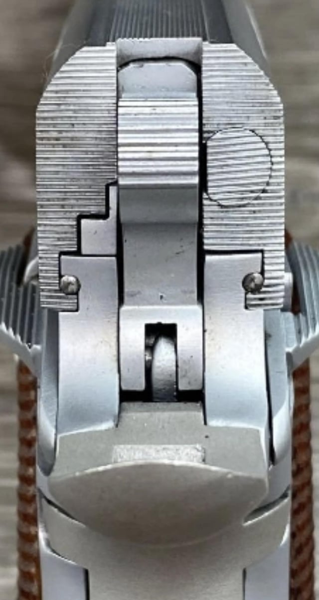 Top-down close-up of a stainless 1911 frame showing machined slide rails, barrel link pin, and thumb safety detent holes.