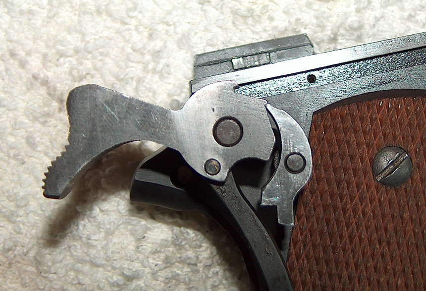 Close-up of a 1911 pistol hammer and sear engagement with action exposed, checkered wood grip panel visible on right