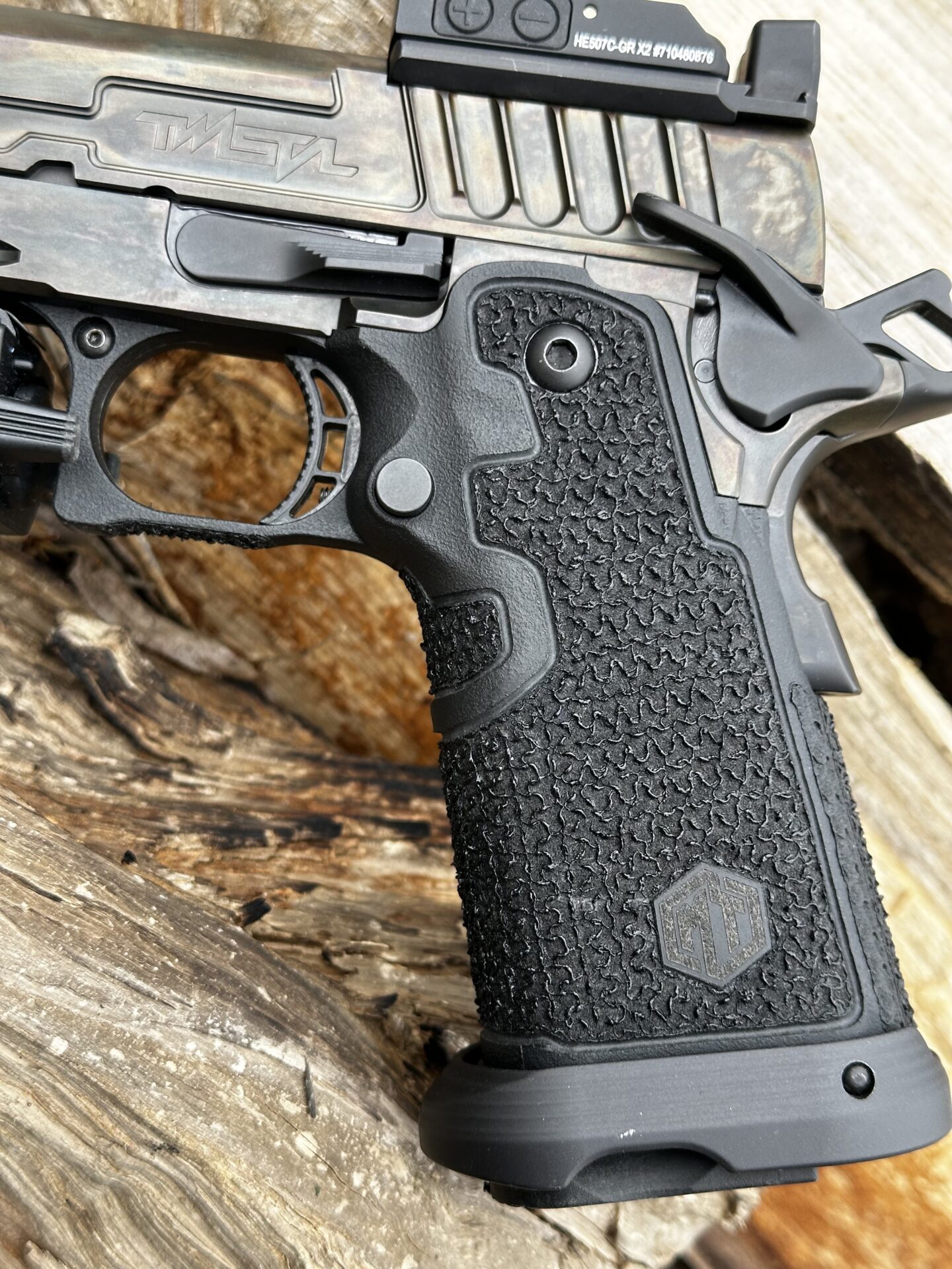 Close-up of a Taran Tactical 2011 pistol grip showing aggressive stipple texture on black grip panels, with a Holosun red dot sight visible on the slide.
